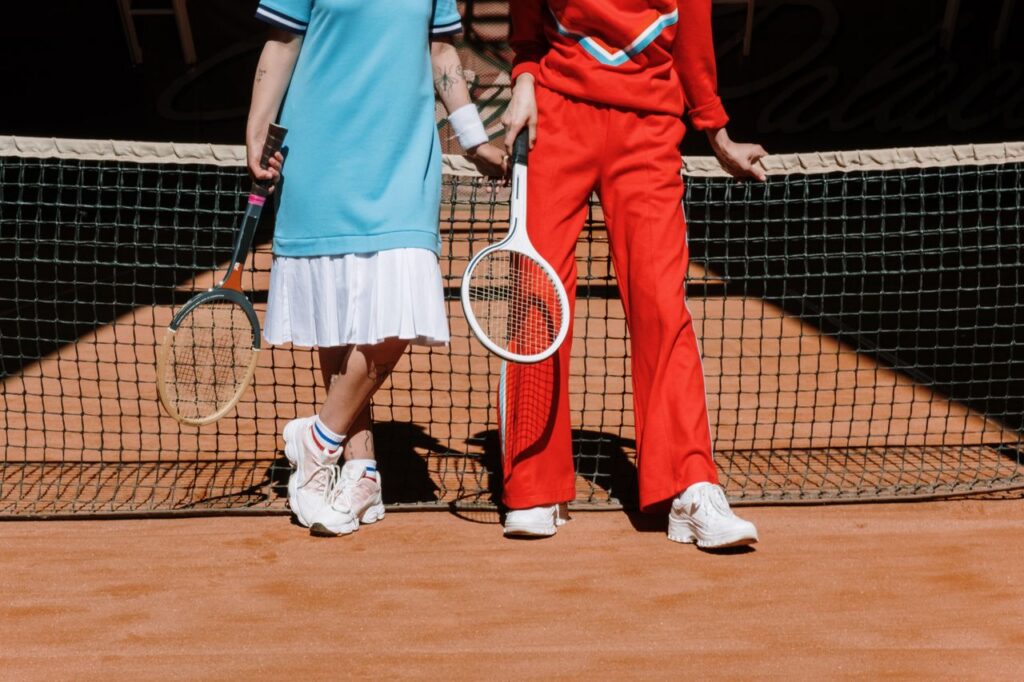 Two tennis players in sporty outfits standing at the net on a clay court.