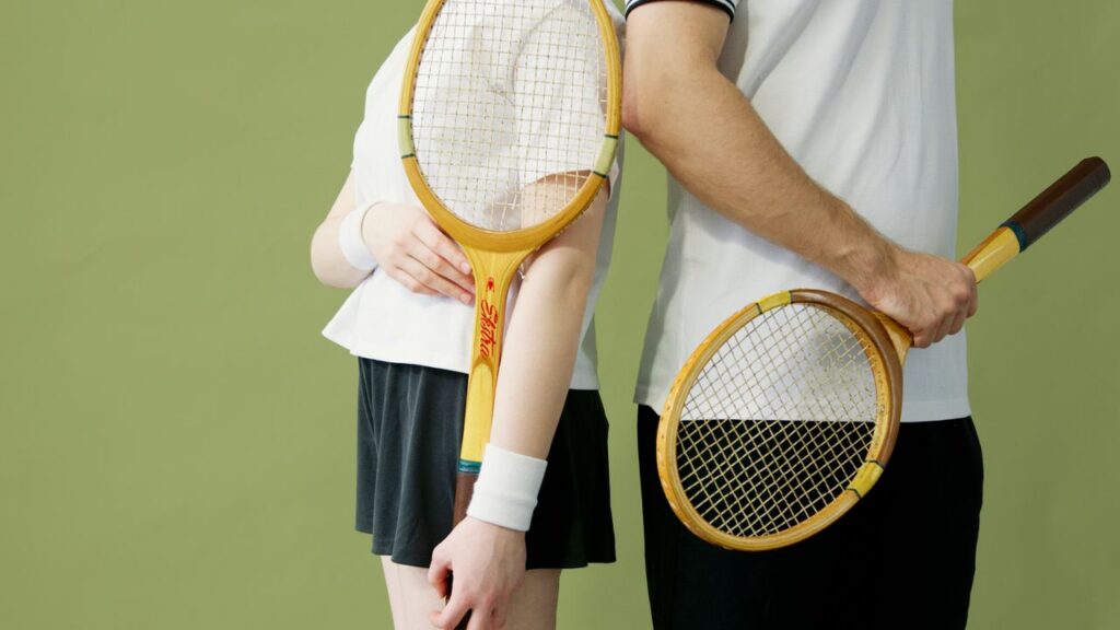 Close-up of tennis players holding vintage wooden rackets against a green backdrop.