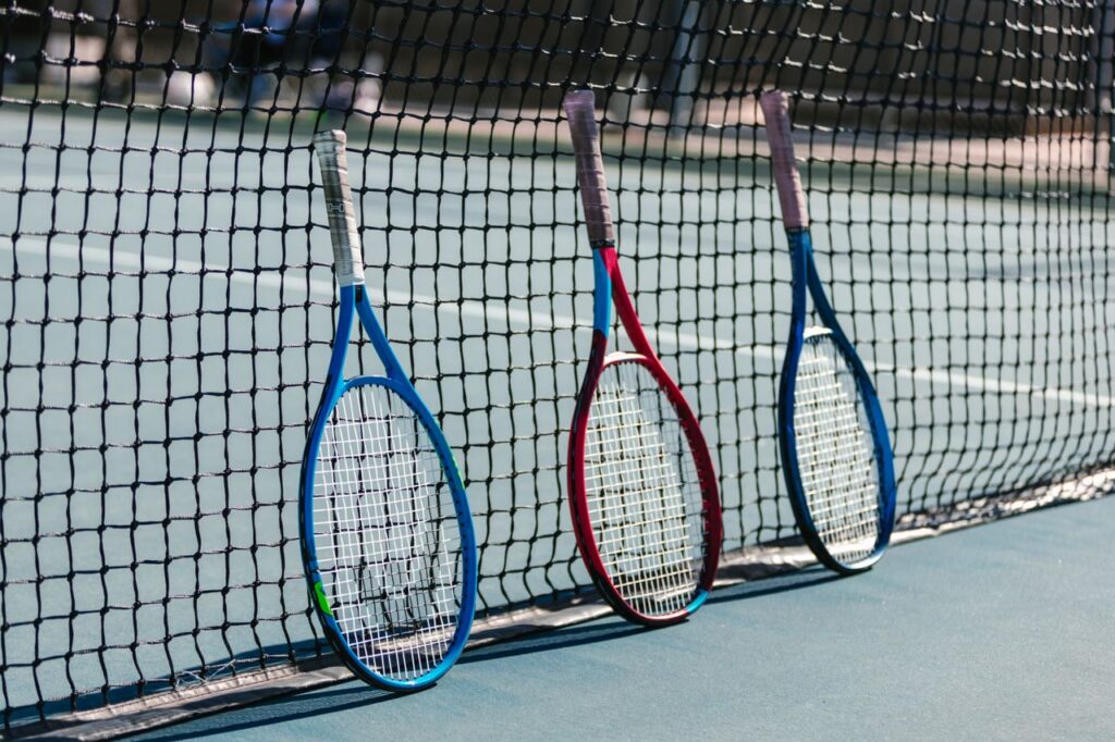 Three colorful tennis rackets leaning against a net on an outdoor tennis court.